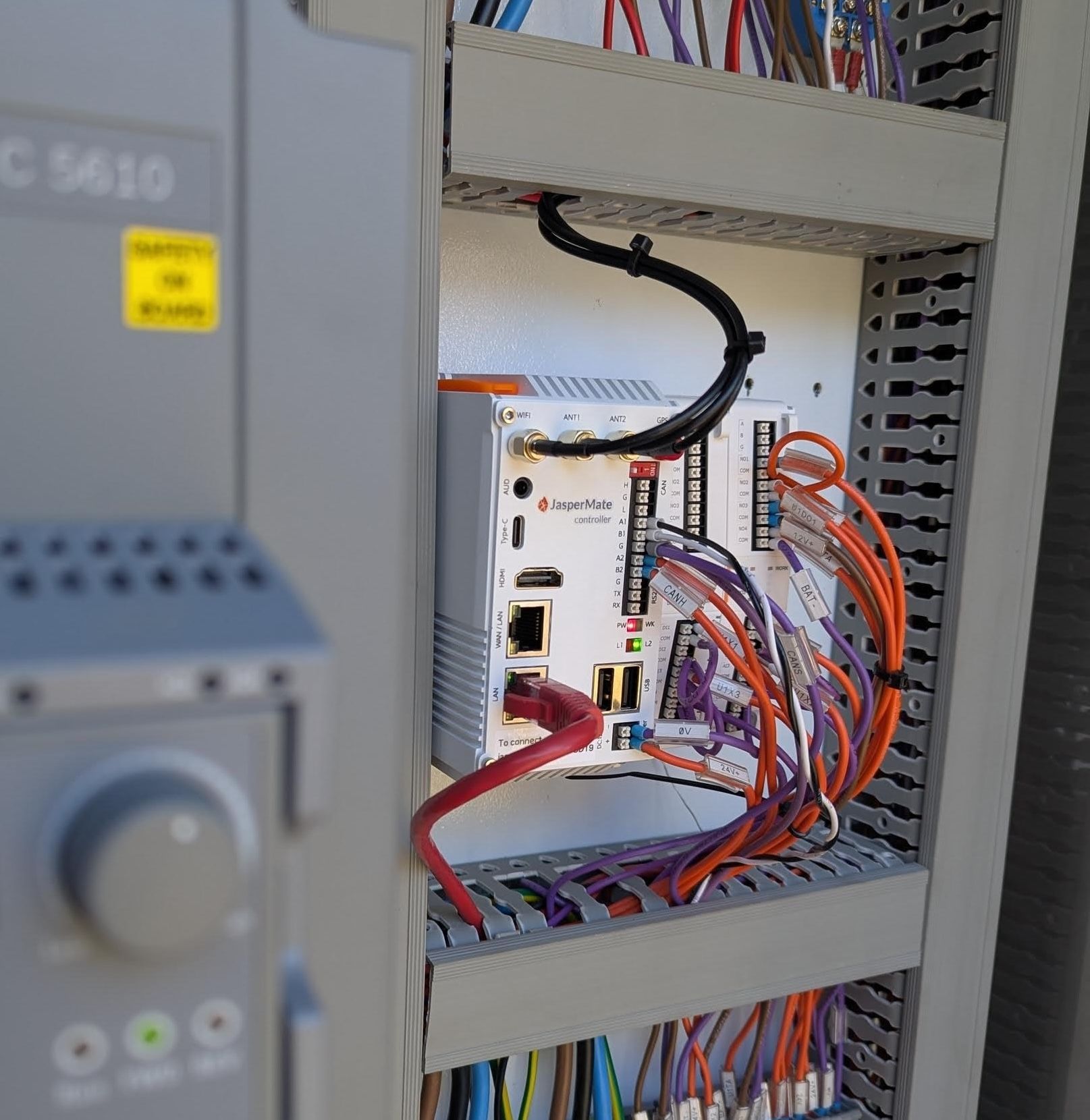 A JasperMate wired into a control panel on site, between cable ducts, with its antenna and Ethernet leads in